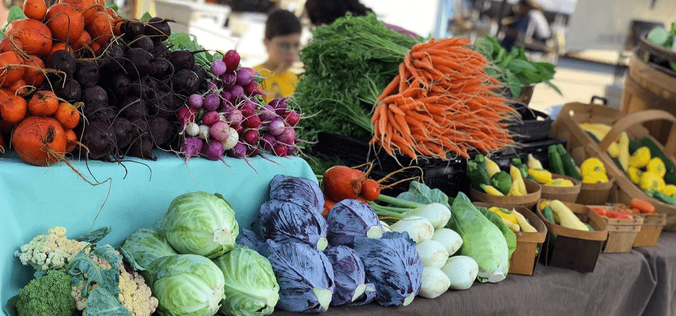 Image of brightly colored vegetables lined up on a table at the Waco Downtown Farmers' Market
