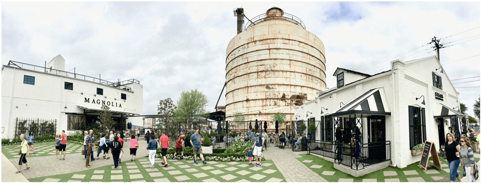 Image of Magnolia Market in Waco, TX. A silo appears in the background, with two white buildings in the foreground: the bakery and market. People are milling about the manicured lawn 
